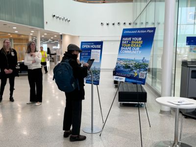Photo of an individual filling out a survey on an iPad with the Unhoused Action Plan branded boards in the background